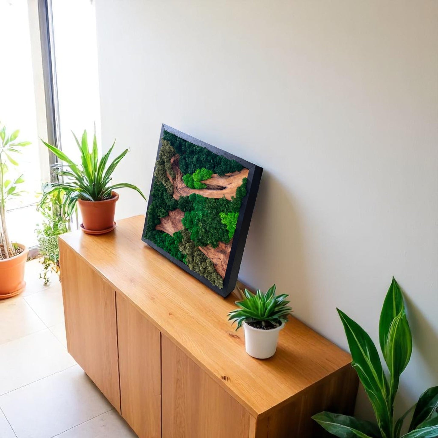 Serenzy Square Moss & Cedar Wall Art with Angled Wood Design leaning against a living room wall on a cabinet with plant decor