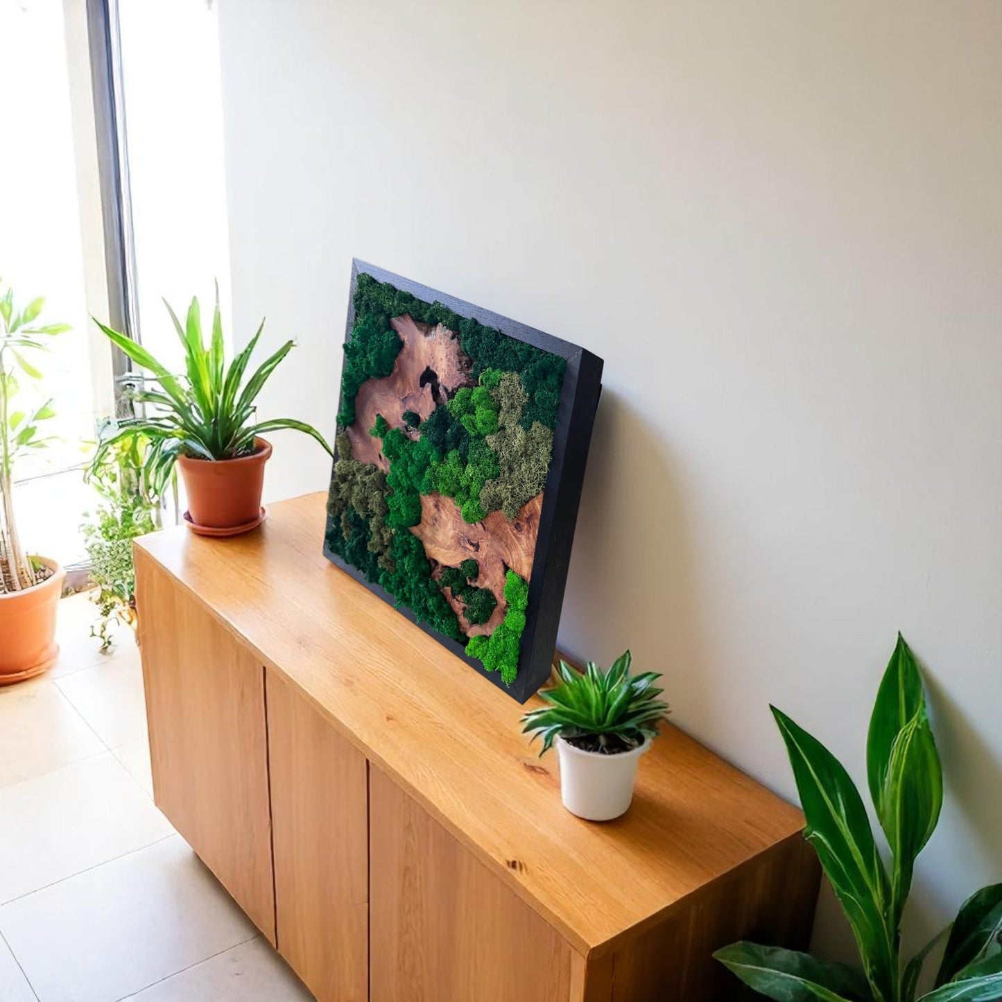 Serenzy Square Moss & Cedar Wall Art with Diagonal Wood Pair leaning against a living room wall on a cabinet with plant decor