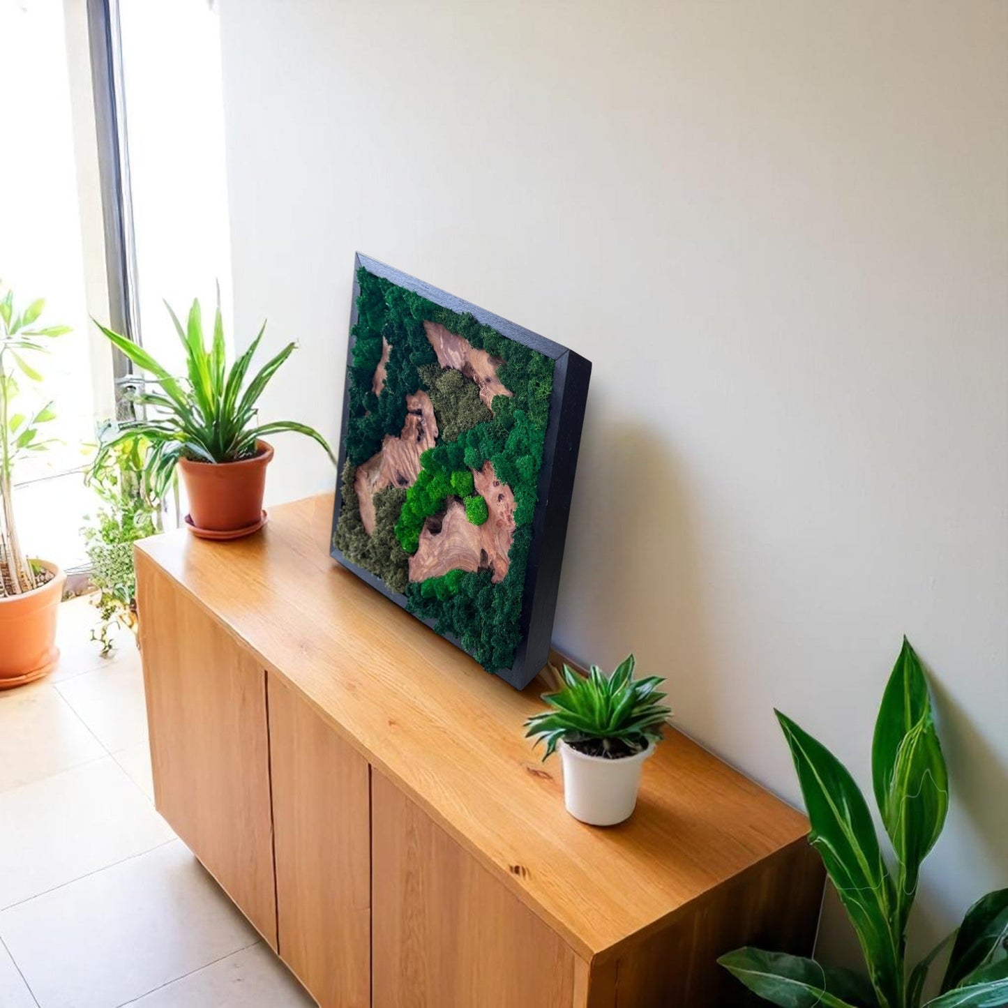 Serenzy Square Moss & Cedar Wall Art with Natural Scattered Wood leaning against a living room wall on a cabinet with plant decor
